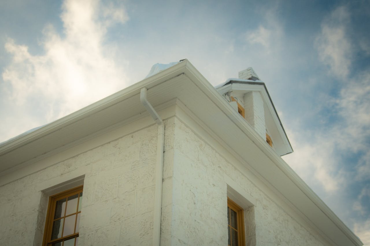 Home A vintage house with an elegant gable roof viewed from below against a partially cloudy sky.