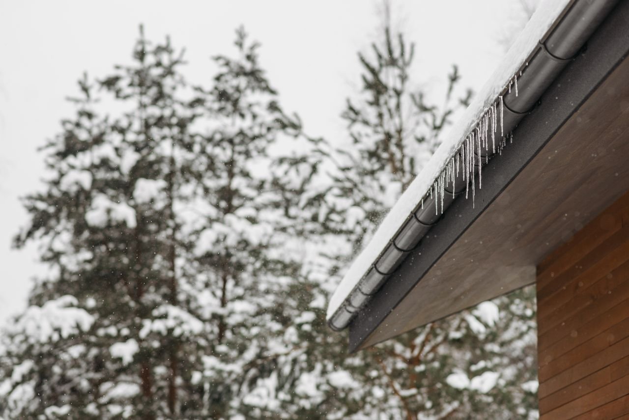 Home Stunning winter scene of icicles hanging from a snow-covered roof with snowy pines in the background.